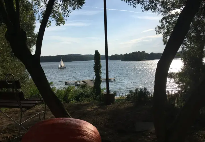 Spokojny dzień nad jeziorem w Puszczy Noteckiej. Żaglówka sunie po wodzie, a na brzegu czeka ławka i wielka dynia.