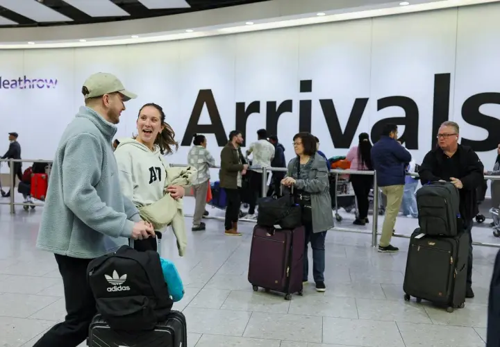 Para podróżnych z bagażami na lotnisku Heathrow, na tle napisu "Arrivals".