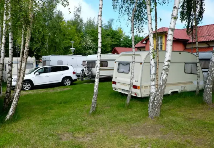 Wesoły camp Polska z przyczepami kempingowymi i białym autem, otoczony drzewami.