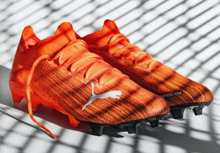 Pomarańczowe korki piłkarskie Puma z napisem "CONTROL PRO". Różnice między korkami profesjonalnymi a amatorskimi są widoczne w technologii i materiałach.