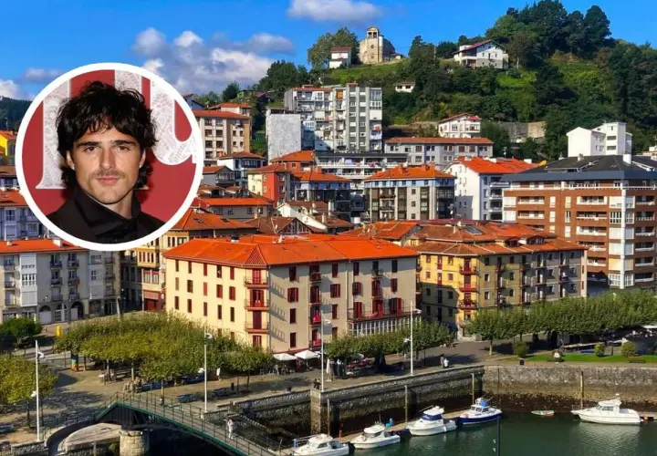 Jacob Elordi, con su aire de galán, posa sobre un pintoresco pueblo vasco con casas de tejados naranjas y un puerto lleno de barcos.