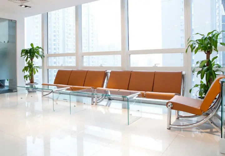 Moderna sala d'attesa con divani in pelle color cuoio, tavolini in vetro e piante verdi. Ottime idee per una sala d'attesa accogliente e di design.