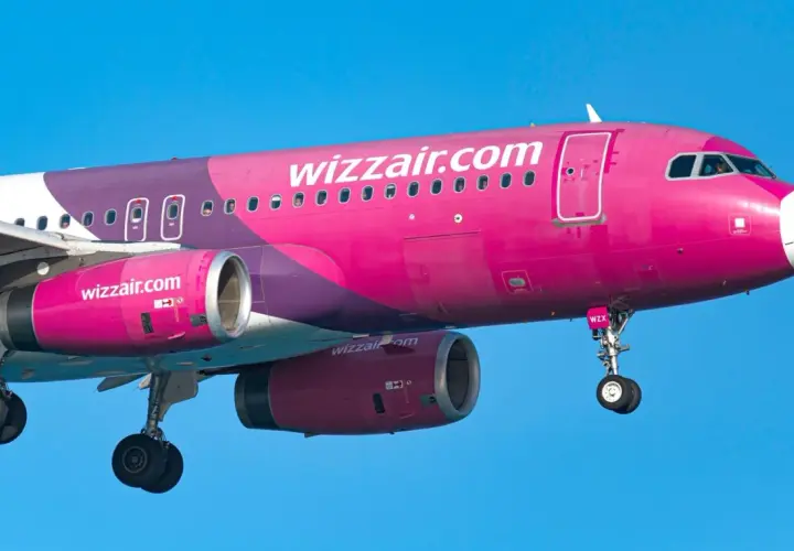 Różowy samolot Wizz Air z widocznymi silnikami i podwoziem na tle błękitnego nieba.