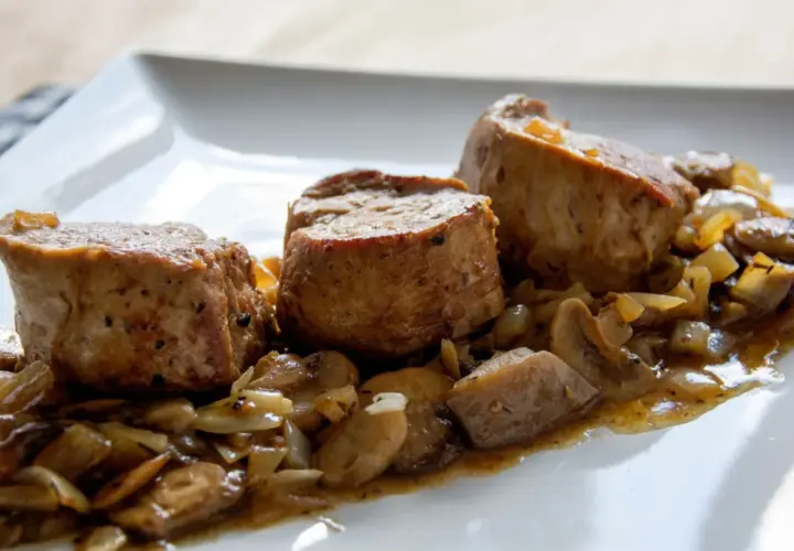 Soczyste polędwiczki w sosie pieczarkowym, podane na białym talerzu. Aromatyczny sos z pieczarkami i cebulką otula delikatne mięso.