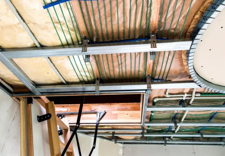 Widok sufitu podwieszanego z widocznymi instalacjami. Widać metalowe profile, wełnę mineralną, rurki systemu ogrzewania podłogowego i elementy konstrukcyjne. Maty kapilarne wady nie są widoczne.