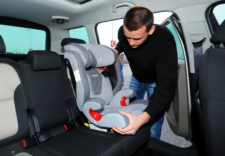 Mężczyzna montuje fotelik samochodowy na bazie Isofix. Czy baza Isofix pasuje do każdego fotelika? Sprawdźmy!