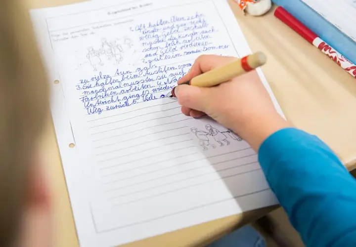 Kind schreibt auf liniertes Blatt. Kleine Zeichnungen illustrieren die Geschichte. Ein typischer Lernmoment im **Wortstamm Grundschule**.