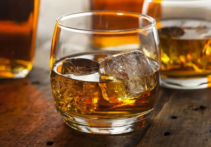 Szklanka whisky z lodem na drewnianym stole. Dowiedz się o różnicy między whisky szkocką a kanadyjską i irlandzką wymogi prawne.
