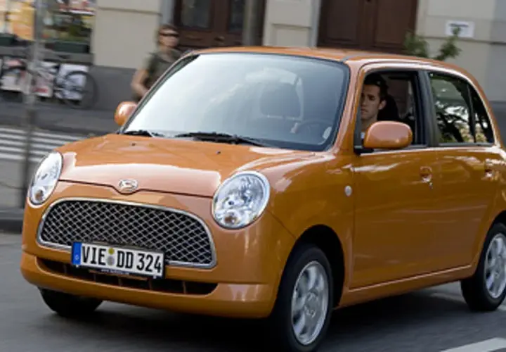 Pomarańczowy Daihatsu Trevis z kierowcą za kierownicą jedzie ulicą.
