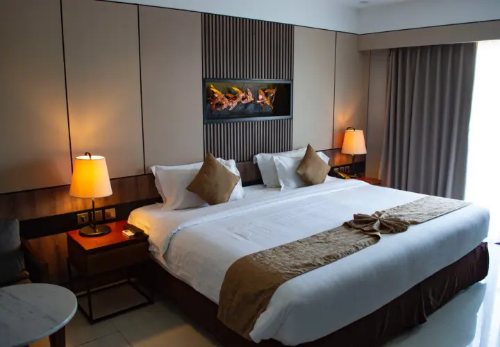 Elegancka sypialnia w stylu hotelowym z dużym łóżkiem, ozdobnym bieżnikiem i obrazem z ptakami nad wezgłowiem.