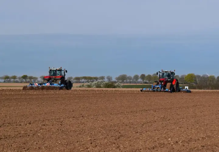 Deux tracteurs préparent le sol pour la culture du lin. Le champ est labouré, prêt pour les semis.