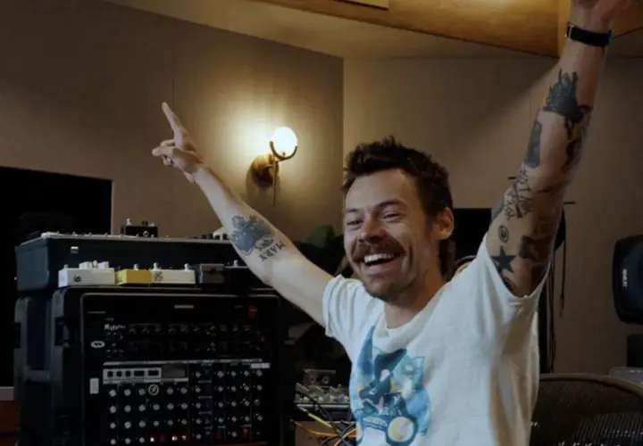 Harry Styles w studiu nagraniowym, z rękami w górze, przygotowuje się do kolejnego koncertu.