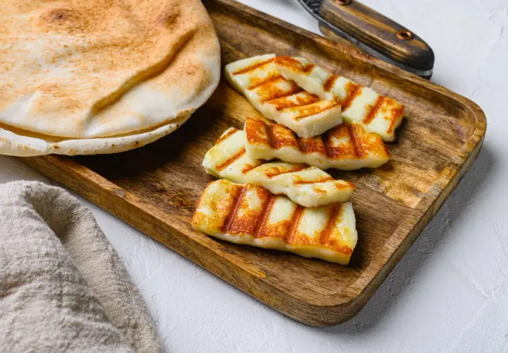 Des morceaux de halloumi grillé, marqués par les rayures du grill, reposent sur un plateau en bois à côté d'un pain pita moelleux.