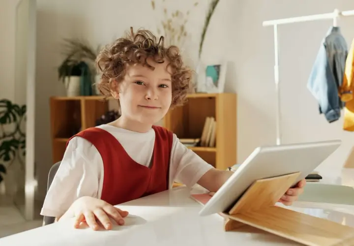 Chłopiec z kręconymi włosami uśmiecha się, trzymając tablet. Czy to wady i zalety szkoły waldorfskiej?