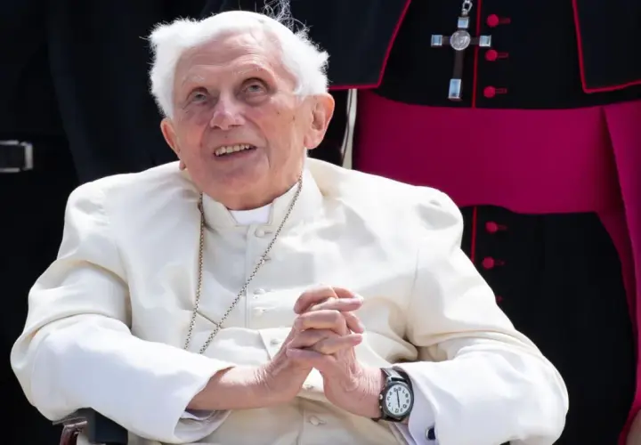 Emeritierter Papst Benedikt XVI. in weißer Soutane, Hände gefaltet, blickt lächelnd nach oben.