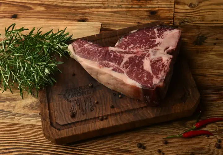 Surowy stek na desce z rozmarynem i pieprzem. Sezonowanie wołowiny na mokro vs na sucho kluczowe różnice w smaku.