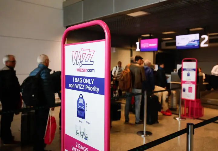 Tablica Wizzair z zasadami bagażu podręcznego, w tle kolejka pasażerów do odprawy.