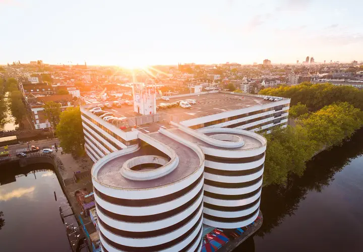 Sonnenuntergang über Amsterdam. Ein Parkhaus mit spiralförmigen Rampen ragt über den Kanal.