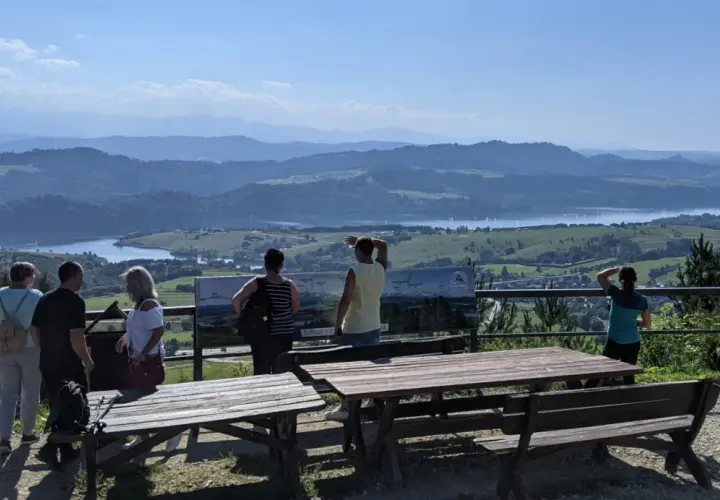 Grupa turystów podziwia rozległą panoramę z widokiem na jezioro i góry. Szlak na górę Wdżar oferuje takie widoki.