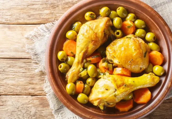Un plat de tajine poulet citron avec des olives vertes et des carottes, servi dans un plat en terre cuite sur une table en bois.