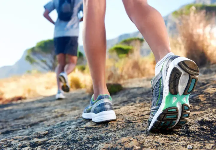 Dwie osoby biegną po kamienistej ścieżce. Zbliżenie na buty biegowe, które są kluczowe, jak przygotować się do biegu na 10 km.