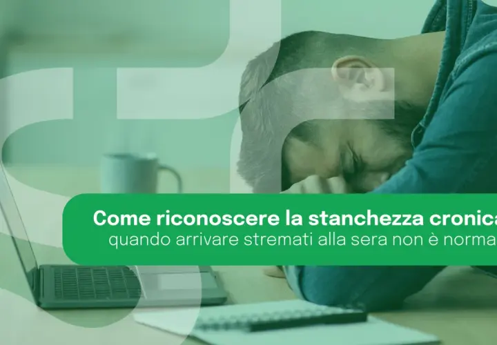 Uomo esausto appoggiato alla mano, con laptop e taccuino. La stanchezza cronica può manifestarsi anche con un senso di spossatezza serale.