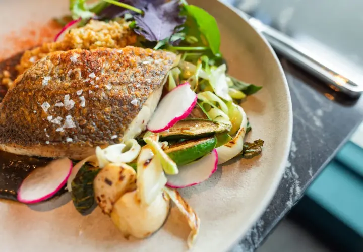 Delicioso pescado blanco crujiente con guarnición de verduras a la parrilla y rábano fresco.