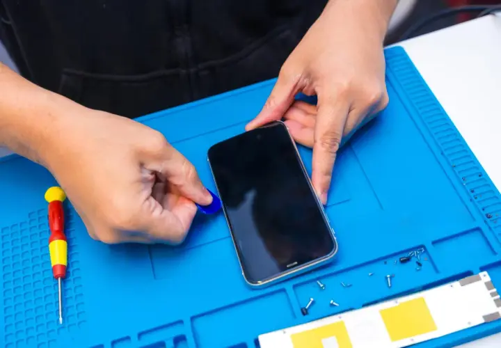 Ręce otwierają telefon, by włączyć nawigację. Obok leży śrubokręt i małe śrubki.