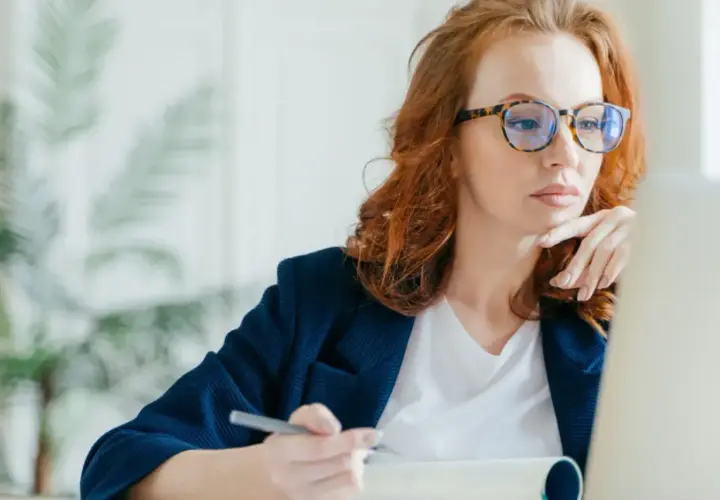 Kobieta w okularach z modną oprawką pracuje przy laptopie. Dofinansowanie do okularów może pomóc w zakupie stylowych i wygodnych oprawek.