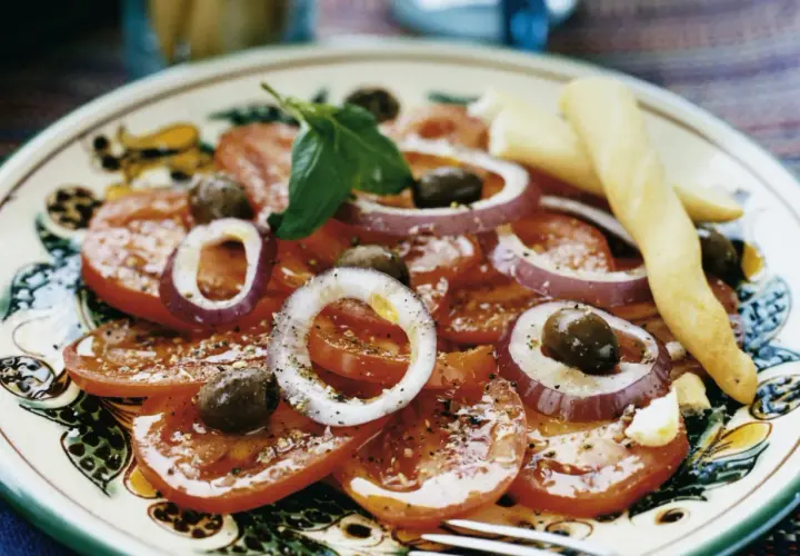 En läcker italiensk potatissallad med tomater, rödlök, oliver och basilika, serverad med grissini.