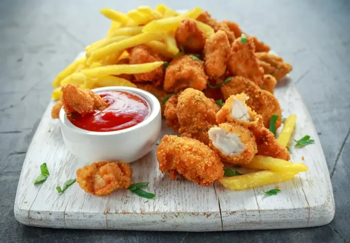 Chrupiące, złociste domowe nuggetsy jak z McDonalda, podane z frytkami i ketchupem na białej desce.