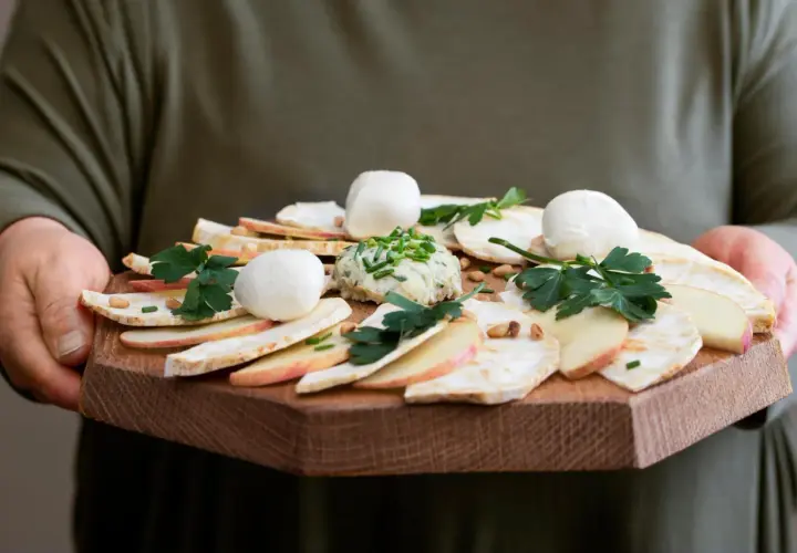 Carpaccio z selera z kulkami mozzarelli, jabłkiem i pastą ziołową na drewnianej desce.