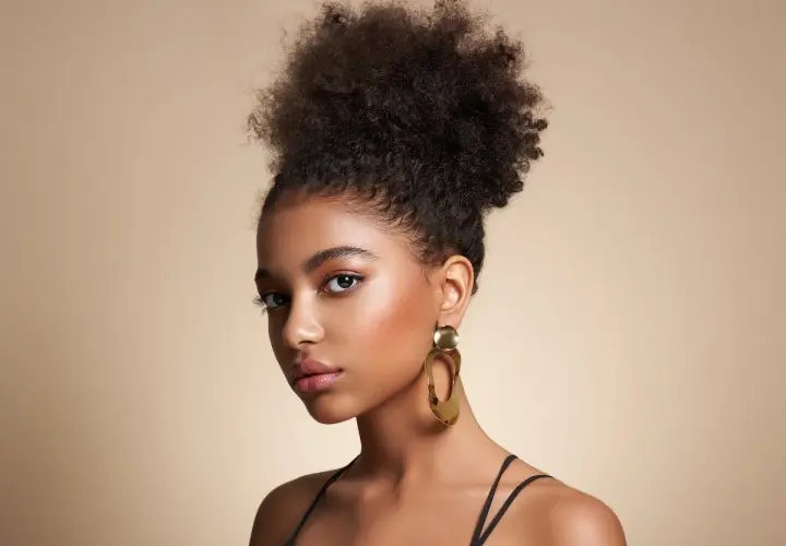 Joven con peinado afro y grandes pendientes dorados, luciendo unos estilos de maquillaje que realzan su belleza natural.