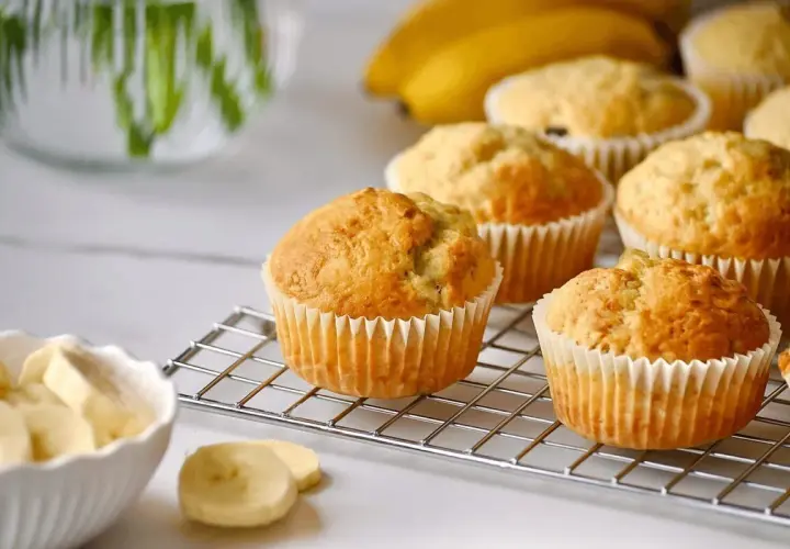 Frisch gebackene bananen muffins auf einem Gitter, daneben eine Schüssel mit Bananenscheiben.