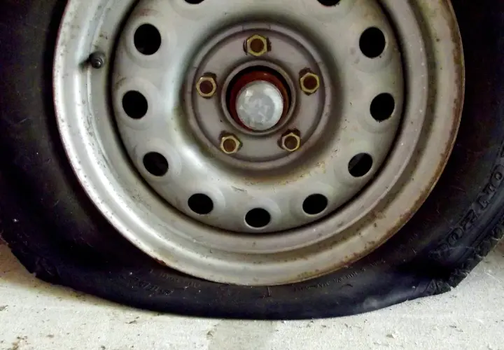 Un clavo en rueda coche ha causado un pinchazo. La llanta metálica y el neumático desinflado se ven sobre el suelo de cemento.