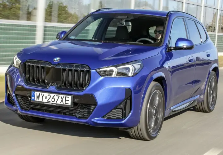 Niebieskie BMW X1 w ruchu drogowym, widok z przodu.
