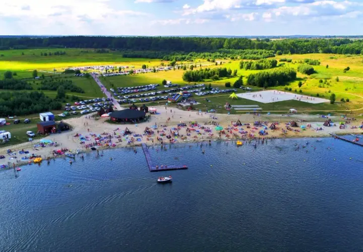Tętniące życiem jeziora na Dolnym Śląsku latem. Plaża pełna ludzi, namioty, parkingi i zieleń wokół.