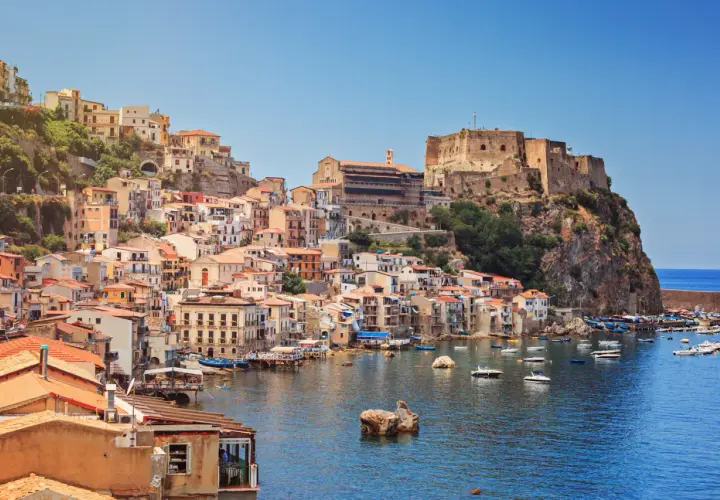 Colorful houses cascade down a cliffside to a harbor filled with boats, overlooking the sea. This is one of the picturesque cities in Calabria, Italy.