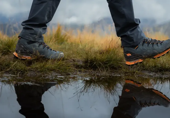 Hiking boots reflected in a puddle. Learn how to get your shoes to stop squeaking on your next adventure.