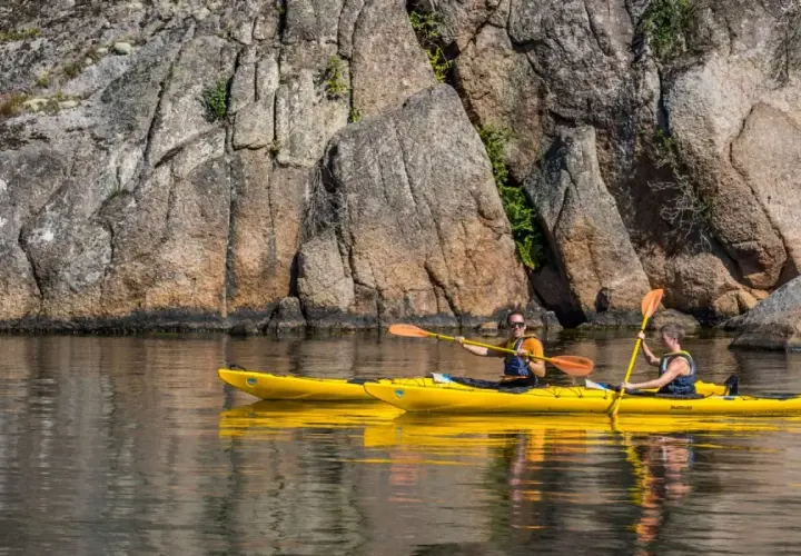 Två personer paddlar varsin gul kajak längs en klippig kust. En härlig dag för upplevelser i Sverige.