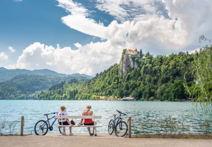 Para odpoczywa na ławce, podziwiając zamek na skale nad jeziorem Bled. Idealne miejsce na camping Bled Slovenia.