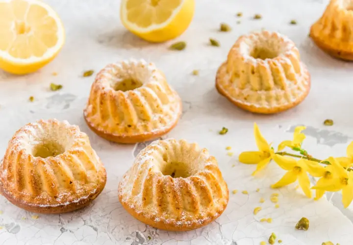 Szybkie babeczki wielkanocne z cytryną i pistacjami, ozdobione cukrem pudrem i gałązką forsycji.