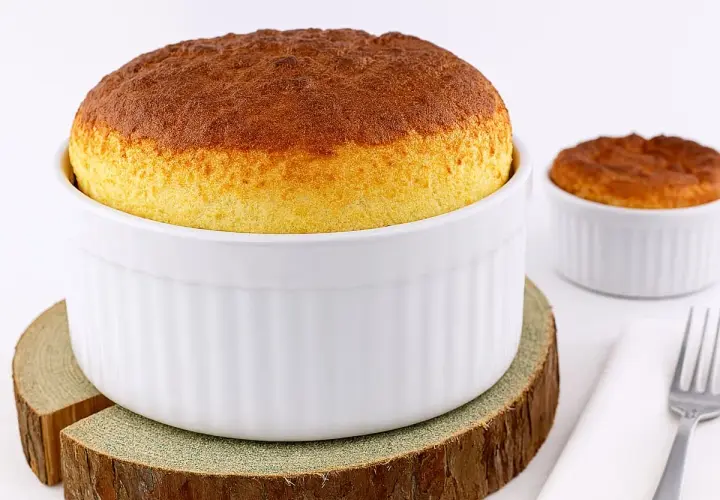 Deux soufflés au fromage dorés, prêts après leur temps de cuisson. L'un est dans un grand ramequin blanc, l'autre dans un plus petit.