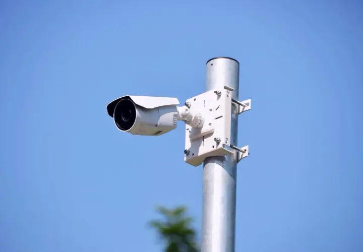 Biała kamera zewnętrzna zamontowana na metalowym słupku, idealna do monitorowania otoczenia. Dowiedz się, jak zamontować kamerę zewnętrzną.