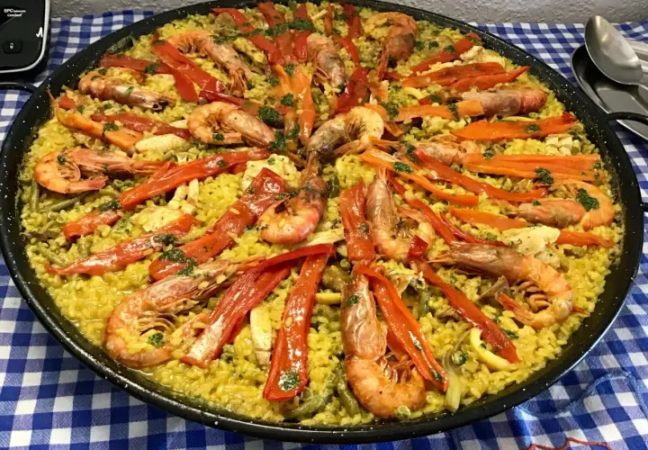 Paella mar y montaña, un festín de arroz amarillo con gambas, pimientos rojos y verduras.
