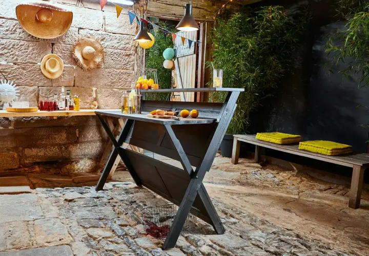 Rustikale Bar selber bauen: Eine dunkle Holzbar mit Orangen und Getränken, dekoriert mit bunten Wimpeln und Hüten. Perfekt für Gartenpartys.