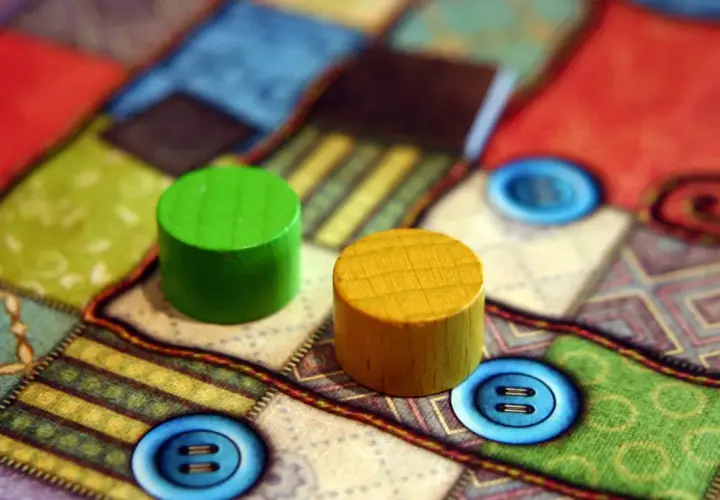 Zwei Holzfiguren auf einem bunten Brettspiel mit Knopf-Symbolen. Perfekt für die besten 2 Spieler Brettspiele.