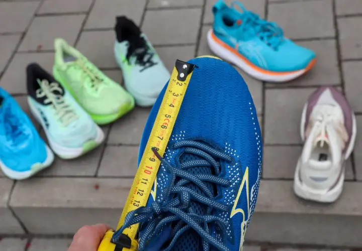 Miarka mierzy niebieskie buty do biegania. Czy buty do biegania powinny być większe? W tle inne kolorowe buty.