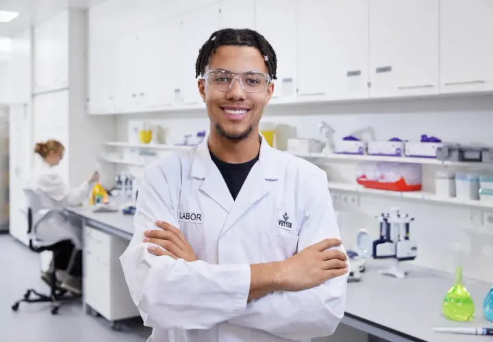Junger Mann im Chemielabor, bereit für neue chemielaborant stellenangebote. Im Hintergrund eine Kollegin bei der Arbeit.