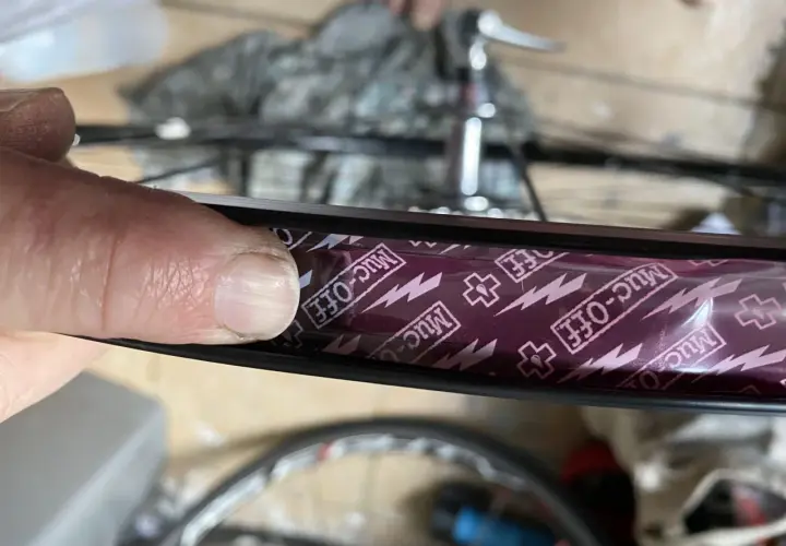 Close-up of a finger pressing down on Muc-Off tubeless rim tape, showing the process of how to tape tubeless rims for a secure seal.
